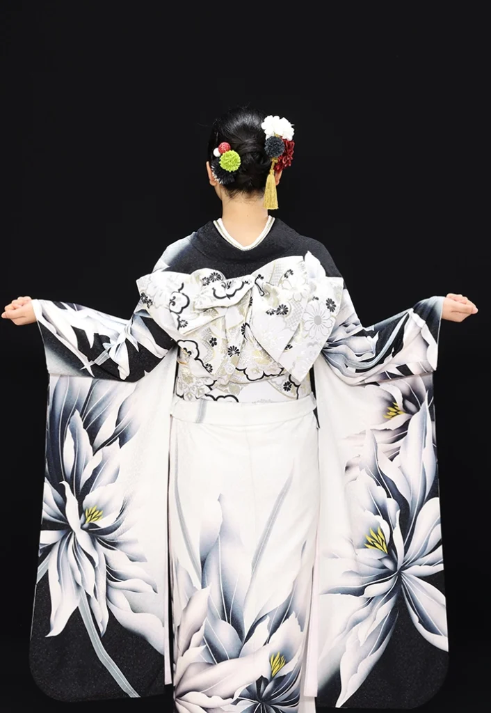 A-24 白銀に大花の振袖後ろ姿｜黒い桜模様の背景にレース柄の帯結びが映えるスタジオ撮影カット