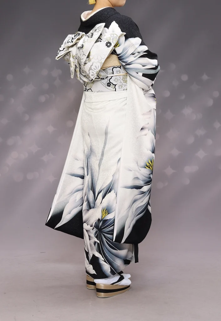 A-24 白銀に大花の振袖後ろ姿｜黒い桜模様の背景にレース柄の帯結びが映えるスタジオ撮影カット