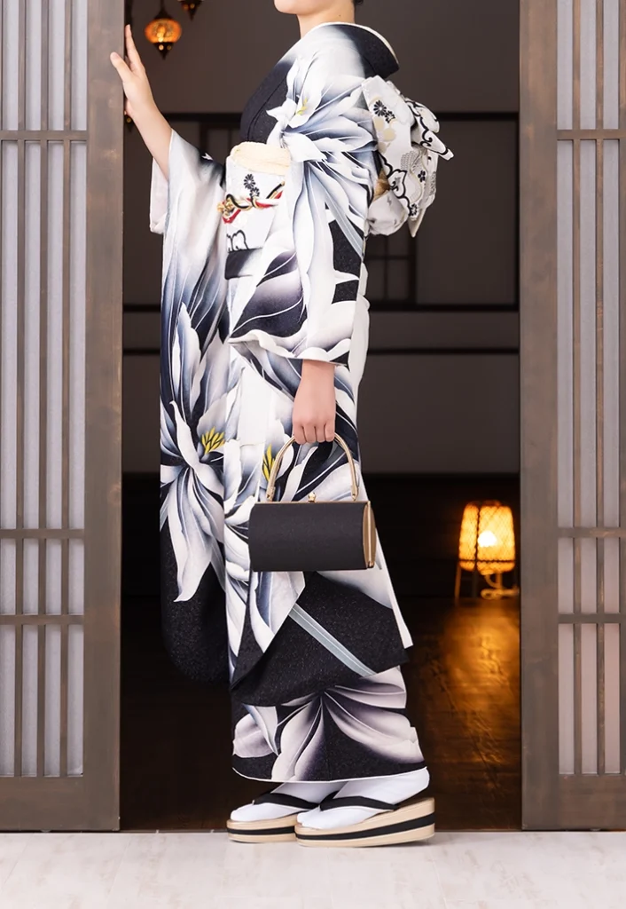 A-24 白銀に大花の振袖を和室の戸口で横向きに立つ全身写真｜大きな花柄の袖と黒いバッグを合わせたコーディネート